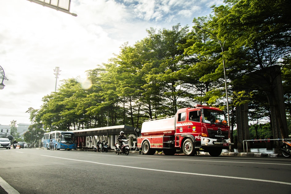 A red truck parks on a street by the trees.