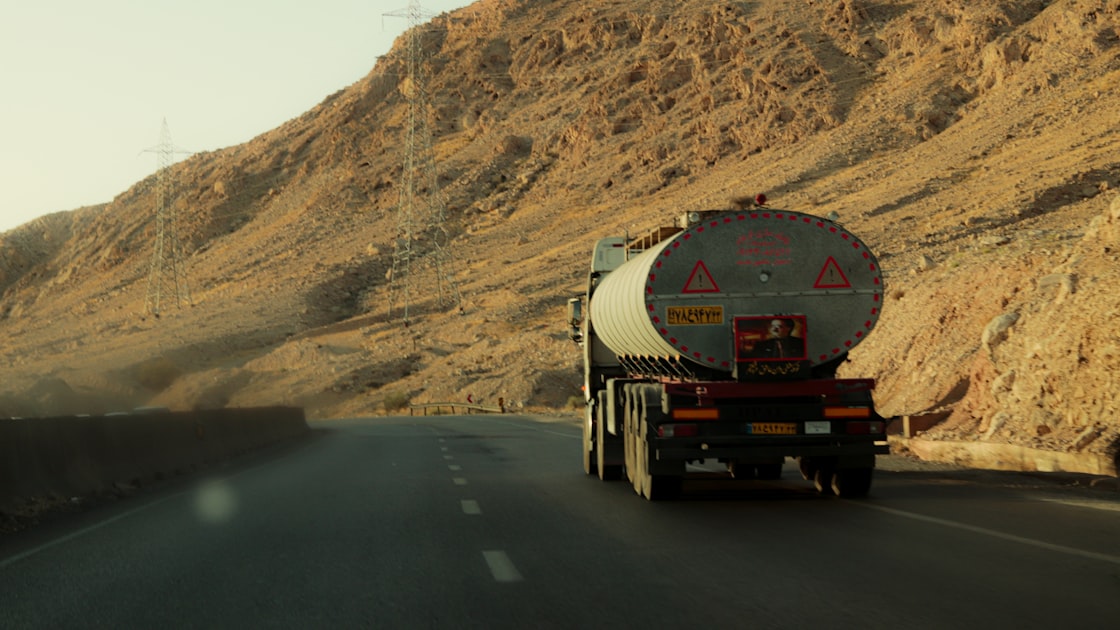 A tanker truck drives on a desert road near mountains