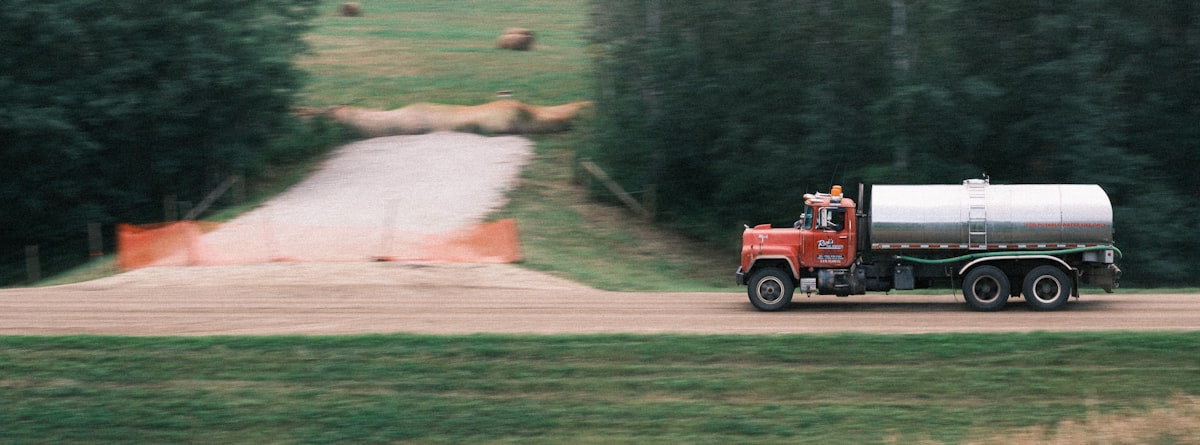 a red truck driving down a road next to a forest