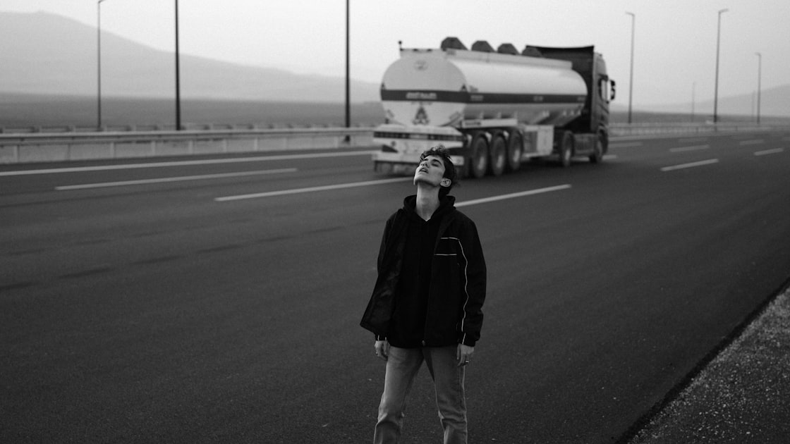 Man looking up on highway with tanker truck.