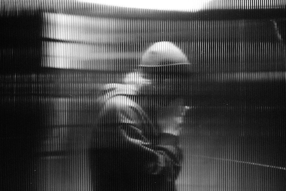 Man in hard hat and hoodie behind vertical blinds