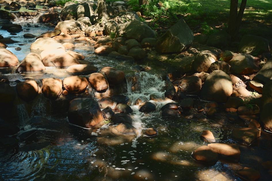 A rocky stream with small waterfalls and dappled sunlight.